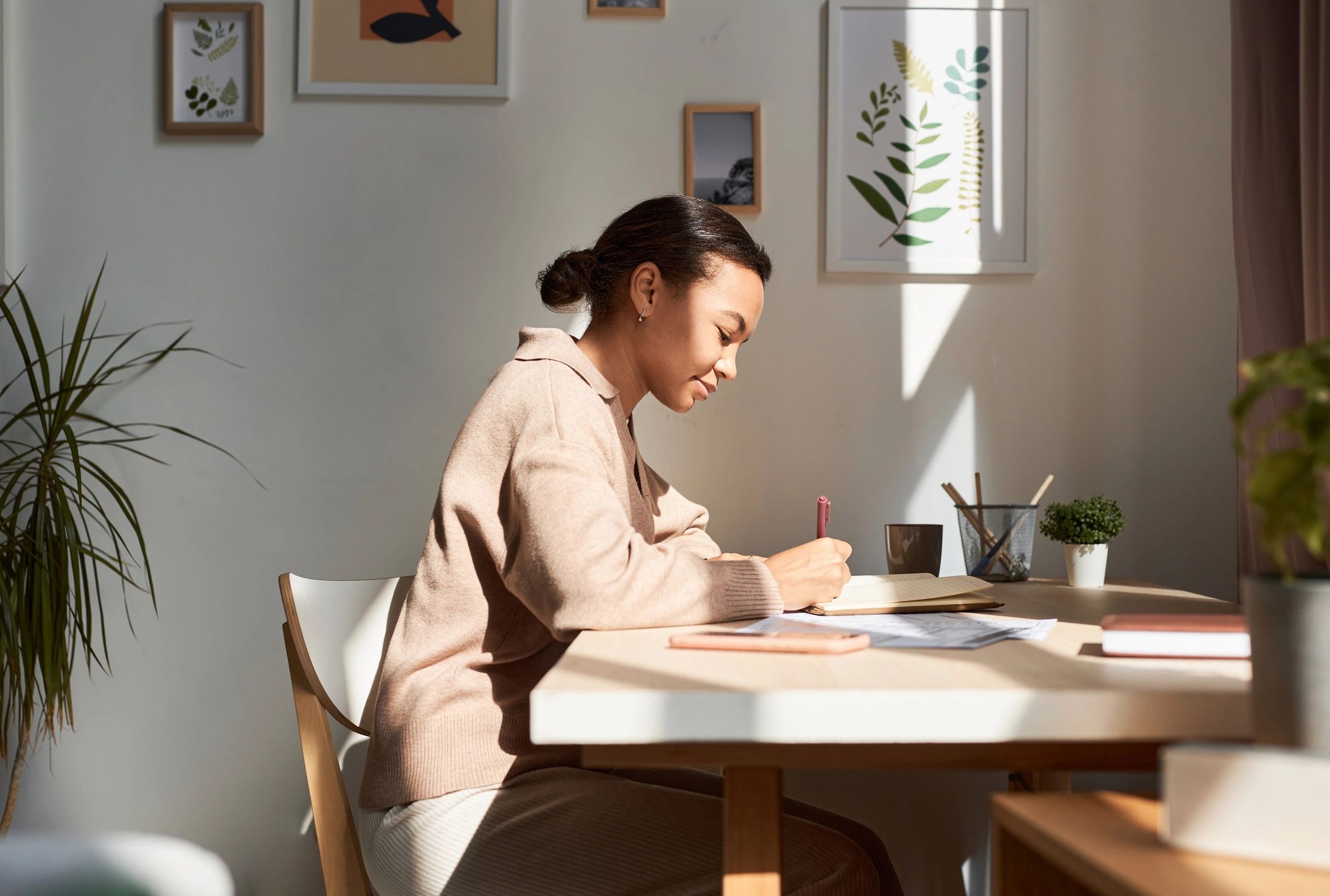 Woman writing in a notebook at a desk with natural light